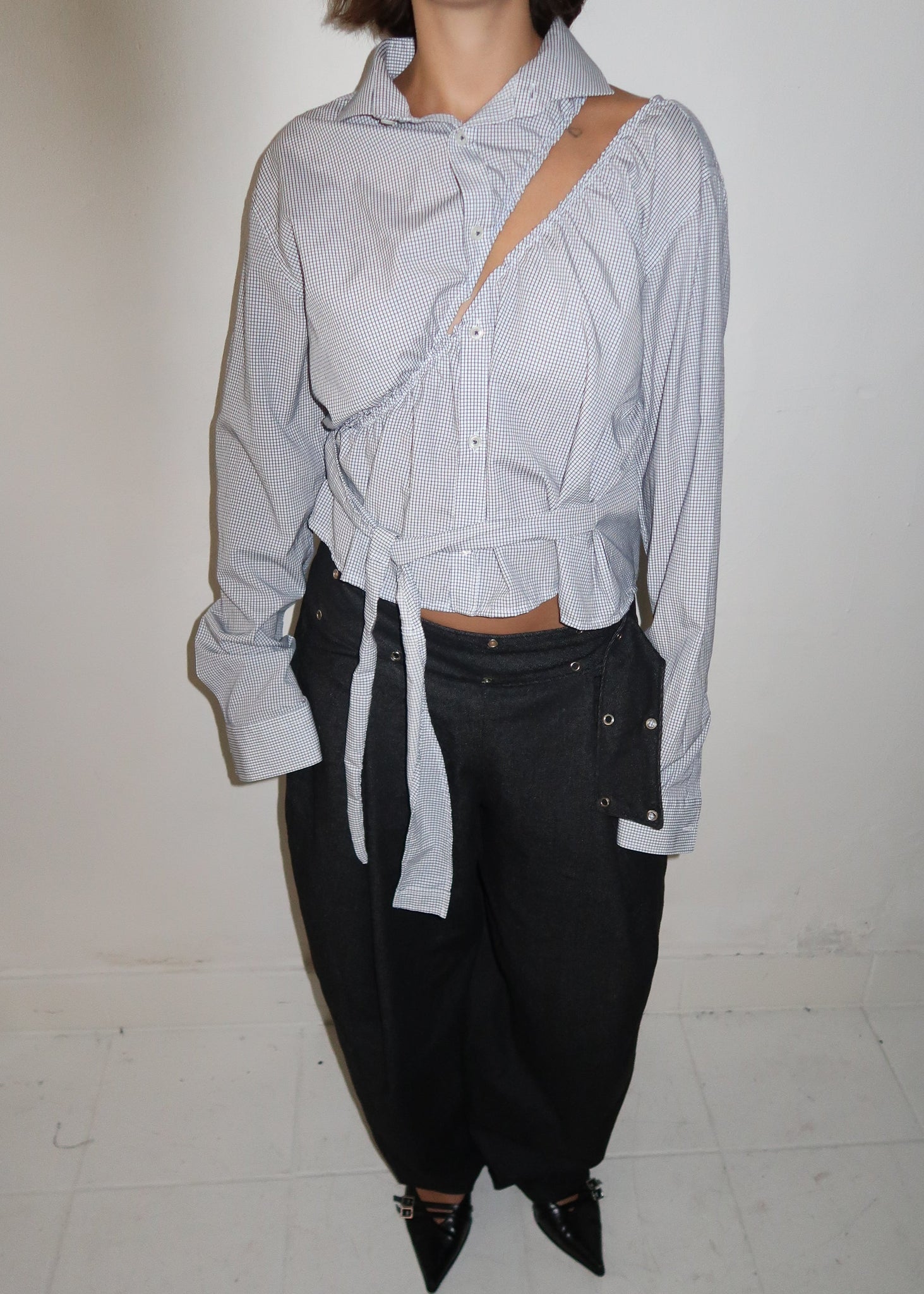 Person wearing a light gray shirt and black pants on a white floor.